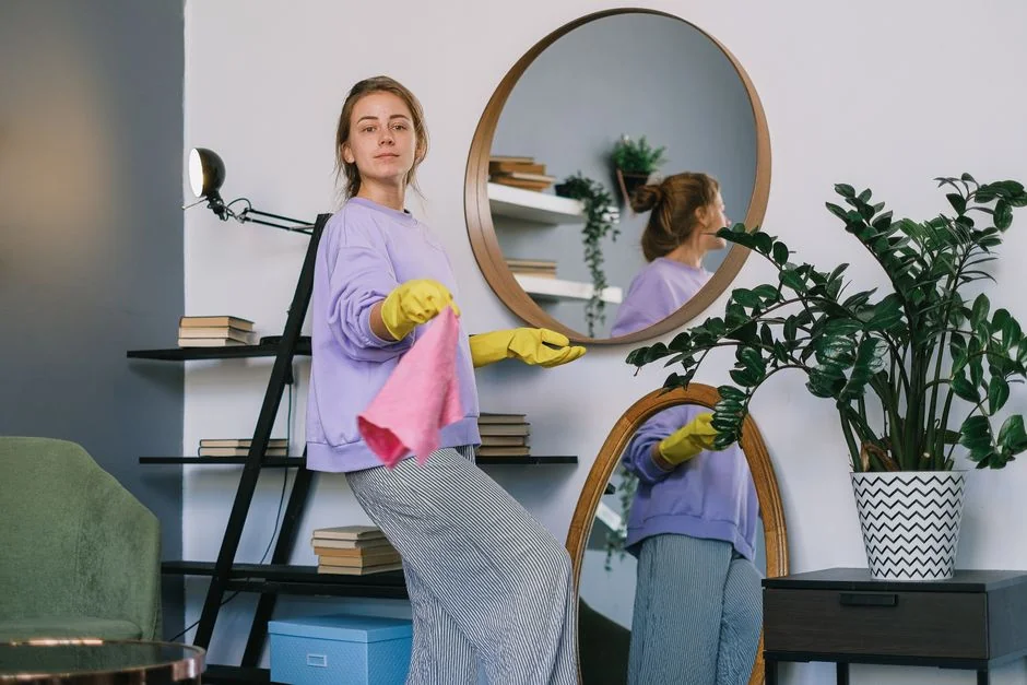 A woman is carefully covering a sofa with protective material while packing boxes in a well-lit room.